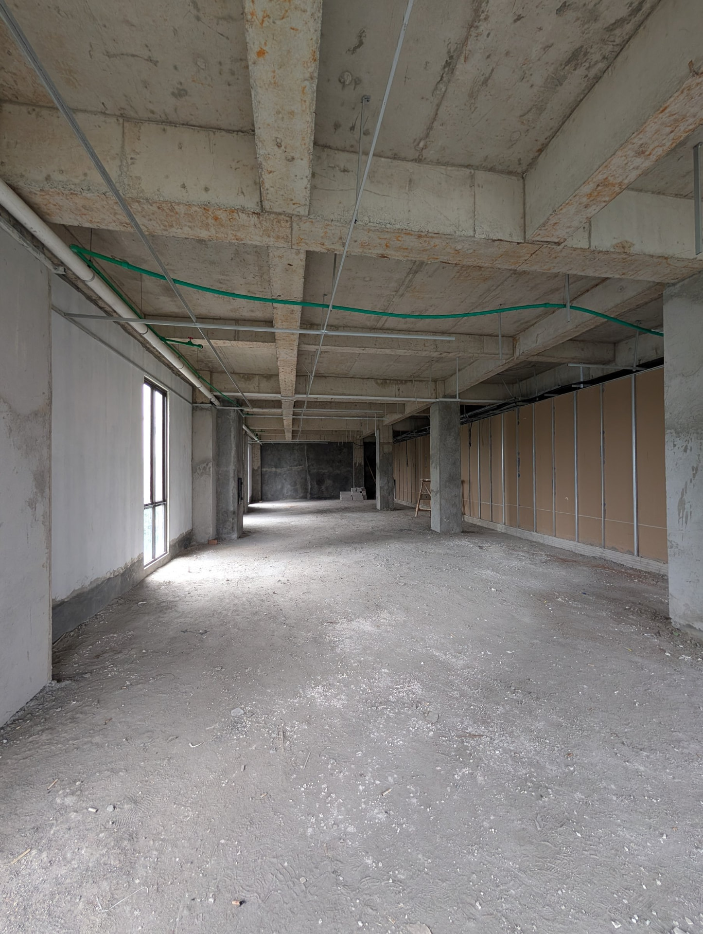 Third-floor space in bare-shell condition with a tall window and exposed concrete ceiling